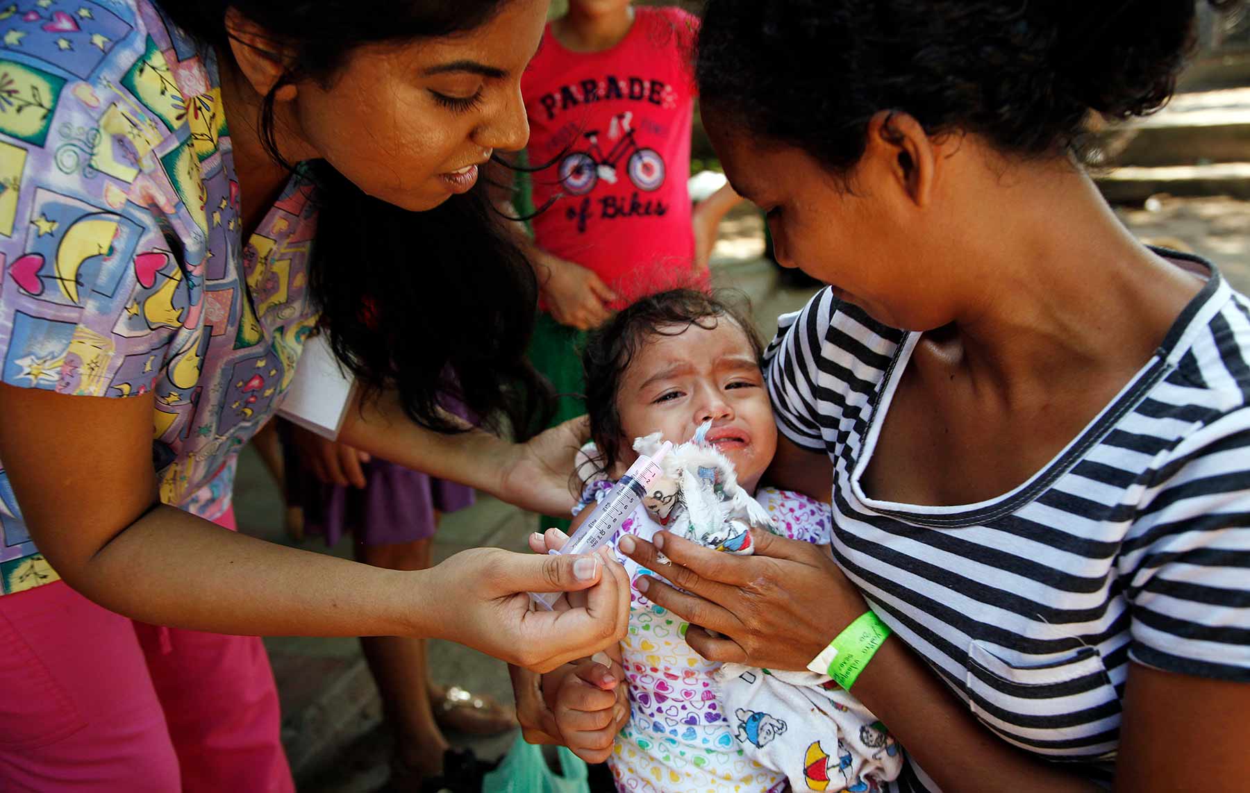 Nursing student Rebecca Sukumar provides medication to a baby who is being comforted by her mother.