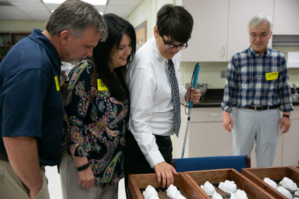Georgia Academy for the Blind student Austin Rogers feels the faces in his 3D yearbook, as his parents (at left) and Dr. Sinjae Hyun with Mercer (right) look on.