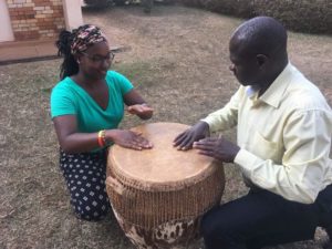 Mercer Peace Corps volunteer Kayla Beasley beats a drum with a man in Uganda.